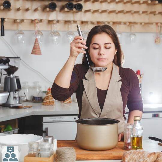 Aspergesoep met vegetarische balletjes, vrouw proeft de soep met een soeplepel, een bruine soeppan staat voor haar op het aanrecht.