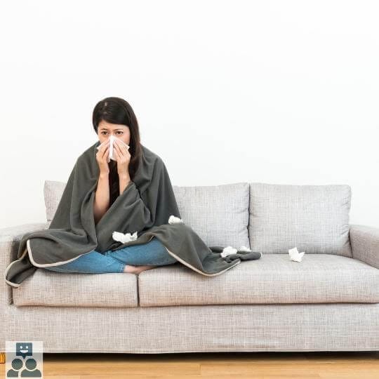 Vrouw zit verkouden op de bank en snuit haar neus met een papieren zakdoek. - Ik Wil Therapie -