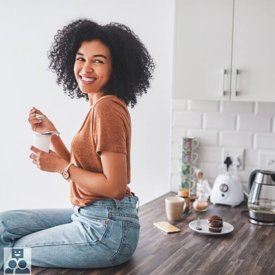 Vrouw eet een bekertje yoghurt , zittend op een tafel