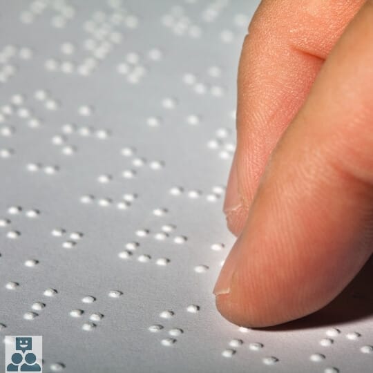 Twee vingers betasren een bel papier met brailleschrift