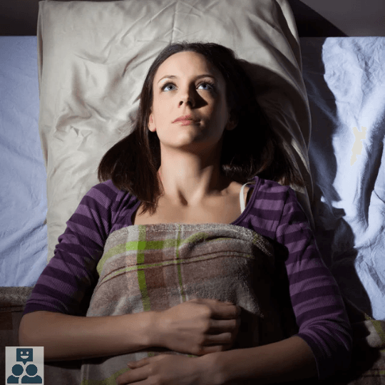 Slaapproblemen, vrouw ligt in bed te staren naar het plafond onder een geruite deken.